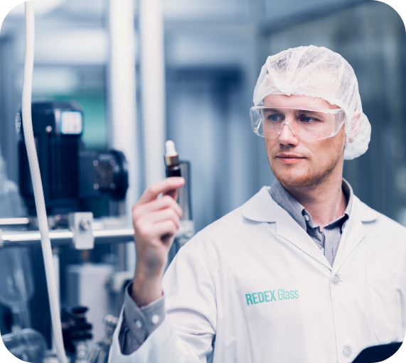 A Redex Glass technician inspecting a dropper bottle in a cleanroom manufacturing environment.