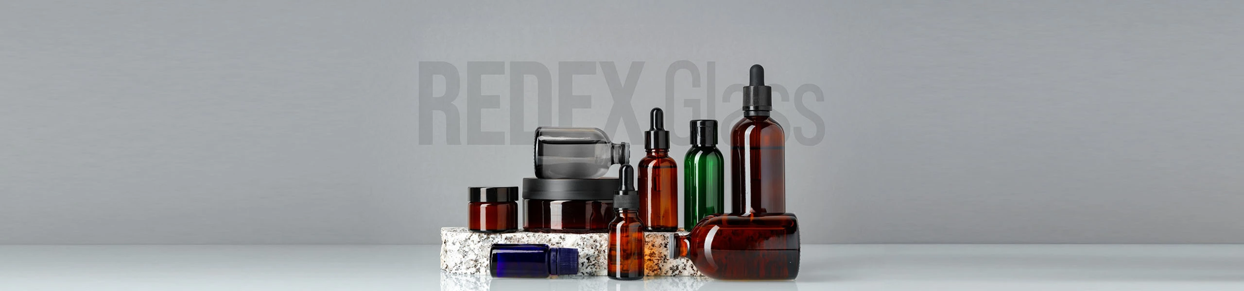 A collection of glass cosmetic bottles and jars in various sizes and colors, including dropper and screw cap types, arranged on marble blocks with 'REDEX Glass' text in the background.